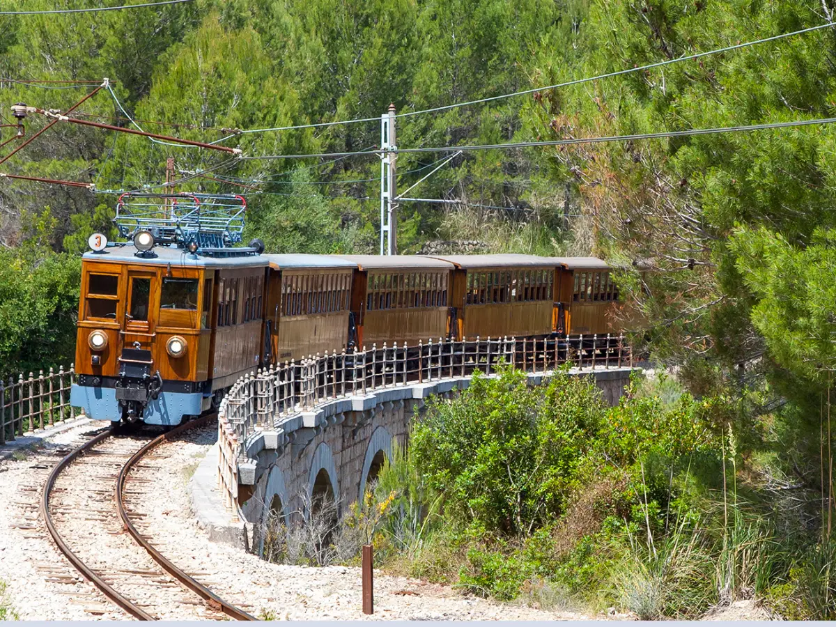 Sóller-toget med trevogner i en sving på en steinbru i skogen over Sóller
